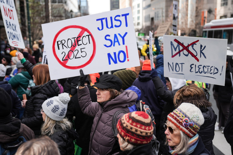 Protestujący demonstrują na zewnątrz, znaki mówią „Projekt 2025, po prostu powiedz nie” i „nie wybrany piżm”